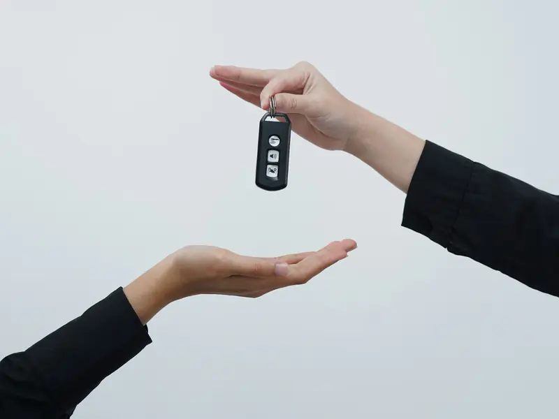 Mão entregando a chave de um carro para outra pessoa