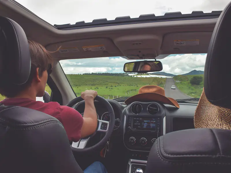 Motorista ao volante em uma estrada, com o campo verde à frente