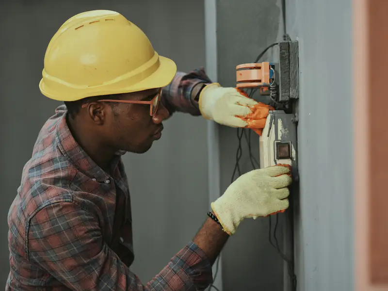 Eletricista com capacete amarelo trabalhando em um quadro de energia